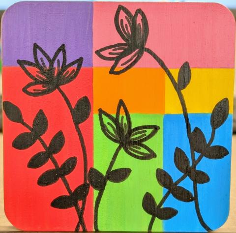 Wooden coaster painted with a rainbow-colored color block background overlayed with black plant silhouettes